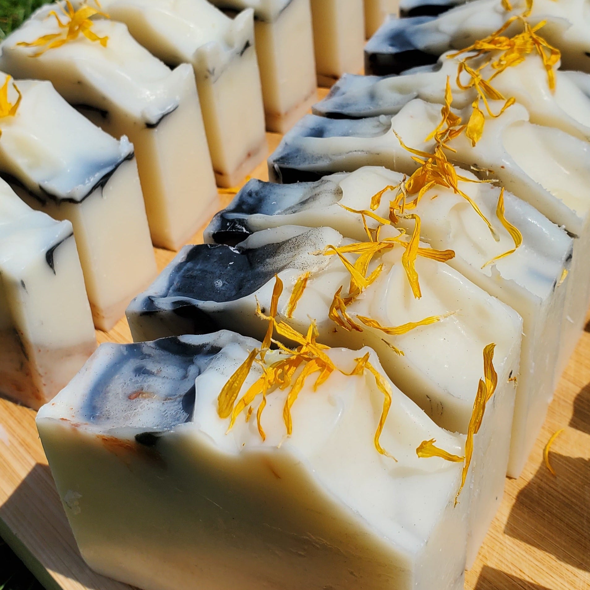 Row of soap bars with orange calendula petals on a wooden board outdoors