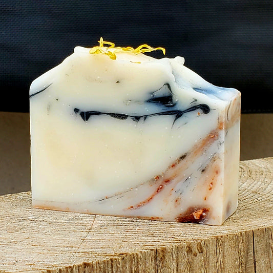 Marble-patterned handmade natural soap bar on a wooden block with a dark background