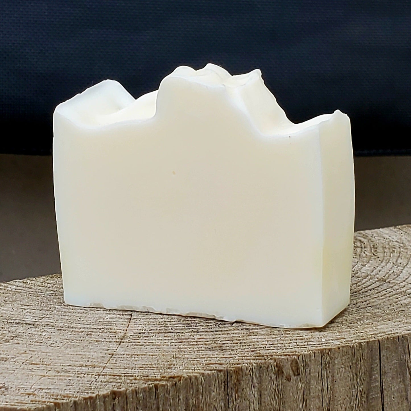 White fragrance free handmade soap bar on a wooden block with a dark background