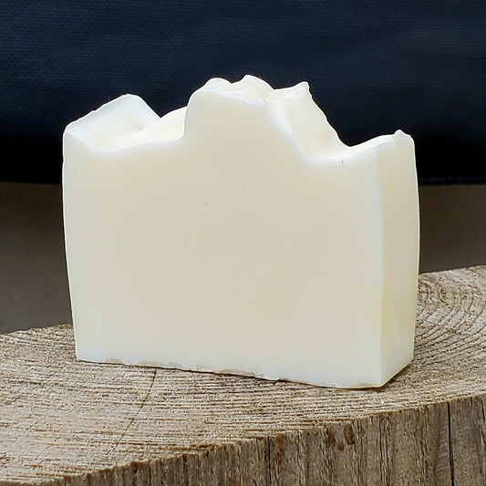 White fragrance free handmade soap bar on a wooden block with a dark background