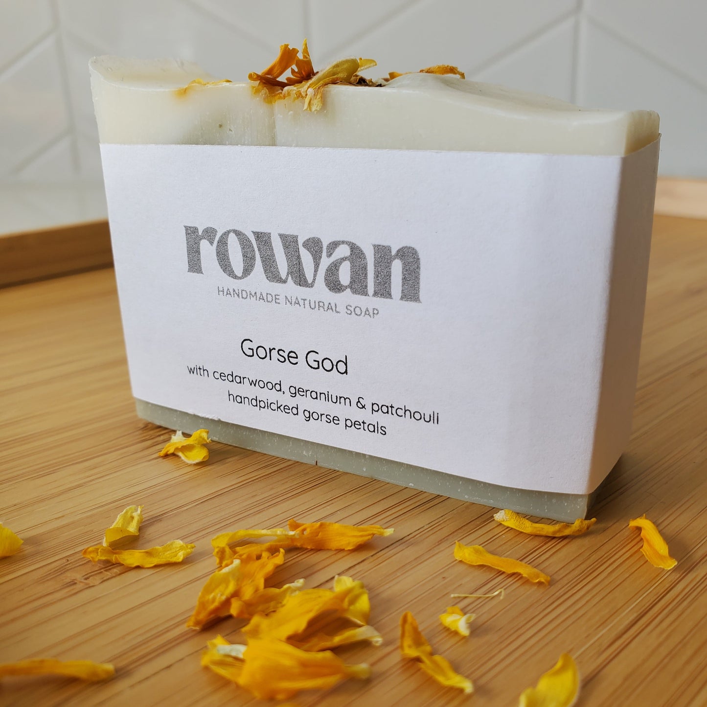 Rowan handmade natural soap bar with yellow flower petals on a wooden surface