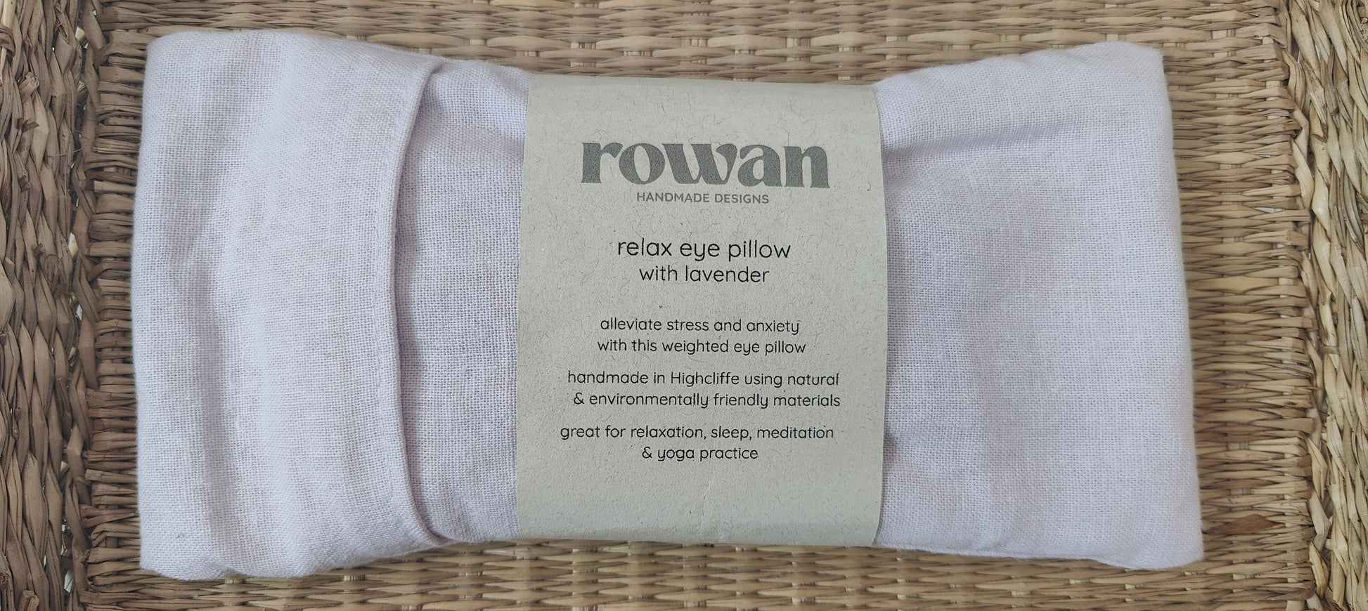 Pale lilac eye pillow with a label on a woven surface