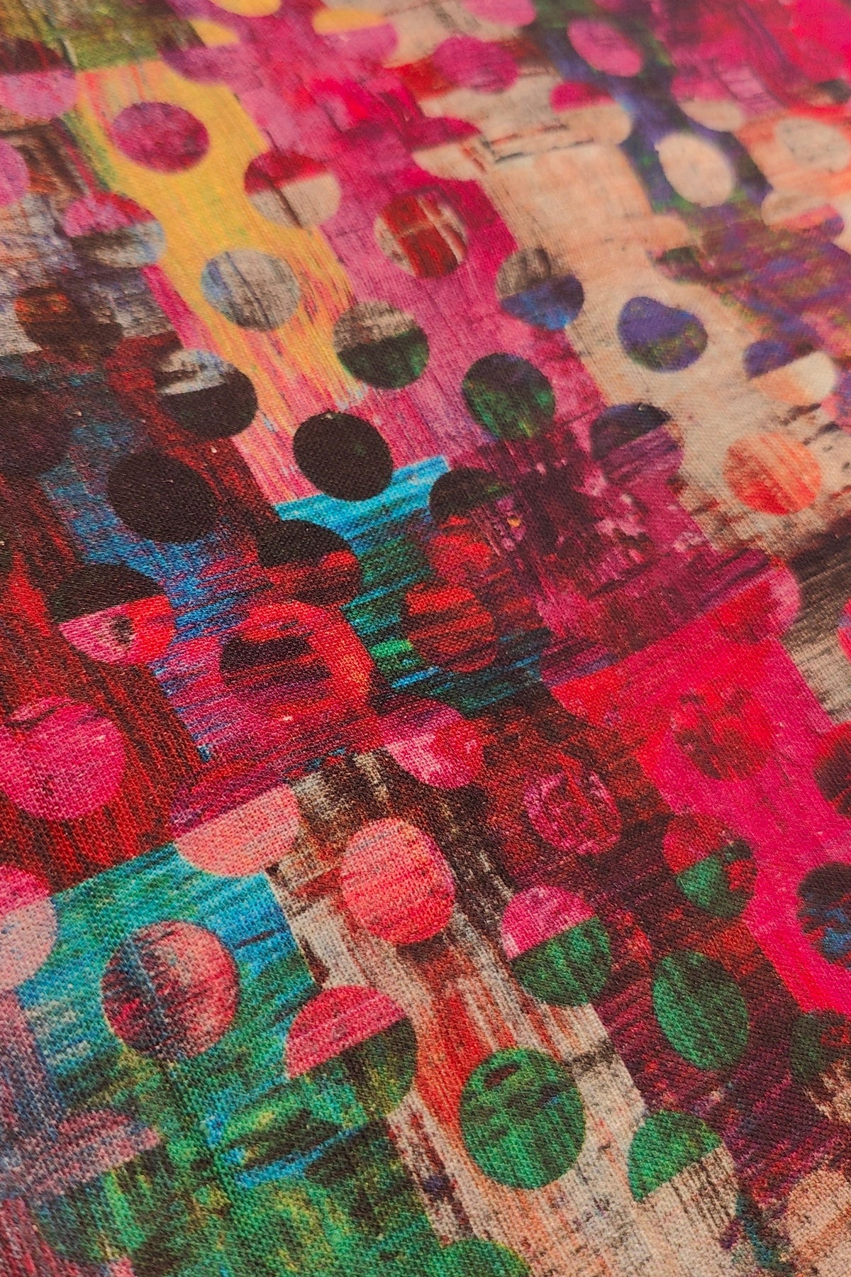 A close-up of a colorful abstract patterned fabric with pink, green, teal, yellow, black, and beige brushstroke-style dots and shapes.